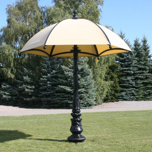 A piece of landscaping, a large elegant umbrella, in a shade of beige, on a black decorative KM pole. The umbrella is located in an open area, amidst nature.